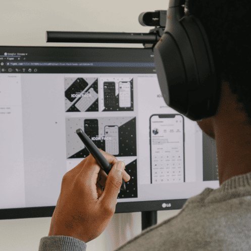 Man met koptelefoon op en pen in zijn hand aan het UX designen op een monitor